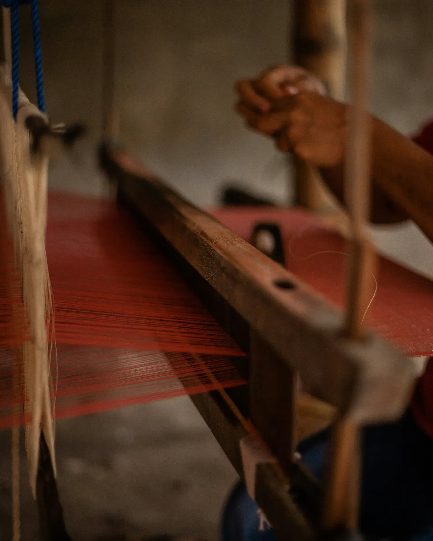 Hands working on a traditional loom with red threads